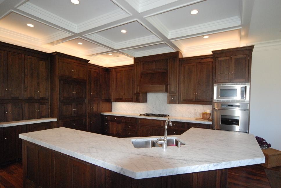 Modern inredning av ett avskilt, stort vit vitt l-kök, med en undermonterad diskho, skåp i shakerstil, skåp i mörkt trä, marmorbänkskiva, vitt stänkskydd, stänkskydd i marmor, integrerade vitvaror, mörkt trägolv, en köksö och brunt golv