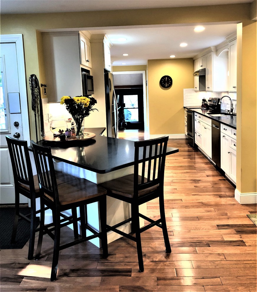 Small transitional galley medium tone wood floor and brown floor enclosed kitchen photo in Boston with an undermount sink, shaker cabinets, white cabinets, granite countertops, white backsplash, subway tile backsplash, stainless steel appliances and black countertops