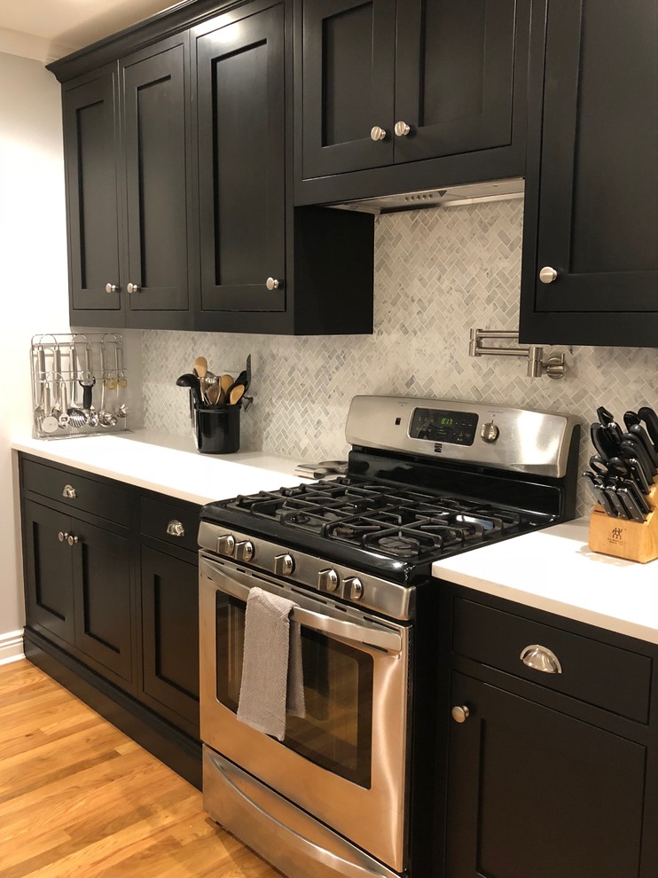 Große Klassische Küche mit Schrankfronten im Shaker-Stil, schwarzen Schränken, Quarzwerkstein-Arbeitsplatte, Rückwand aus Marmor, braunem Holzboden und Kücheninsel in New York