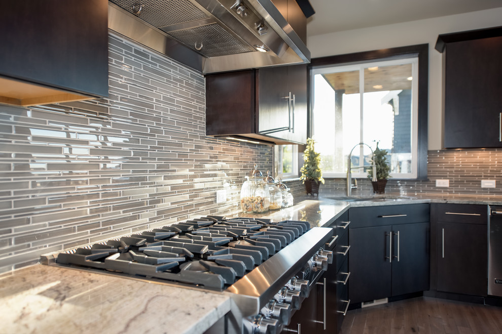 Photo of a contemporary u-shaped open plan kitchen in Seattle with a submerged sink, flat-panel cabinets, dark wood cabinets, granite worktops, grey splashback, glass tiled splashback, stainless steel appliances, medium hardwood flooring and an island.