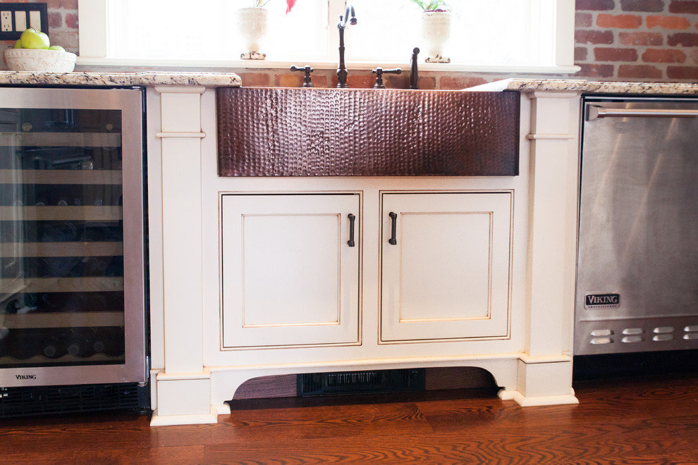 Foto på ett mycket stort lantligt kök, med en rustik diskho, vita skåp, granitbänkskiva, rött stänkskydd, rostfria vitvaror, mellanmörkt trägolv, luckor med profilerade fronter och stänkskydd i tegel