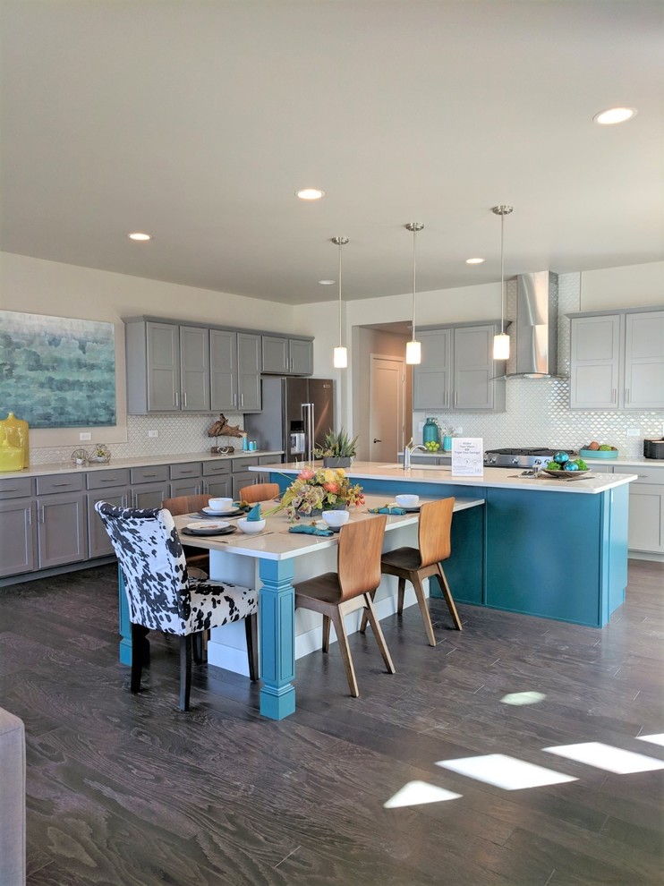 This is an example of a medium sized contemporary l-shaped kitchen/diner in Denver with a double-bowl sink, flat-panel cabinets, grey cabinets, engineered stone countertops, white splashback, ceramic splashback, stainless steel appliances, medium hardwood flooring, an island, brown floors and white worktops.