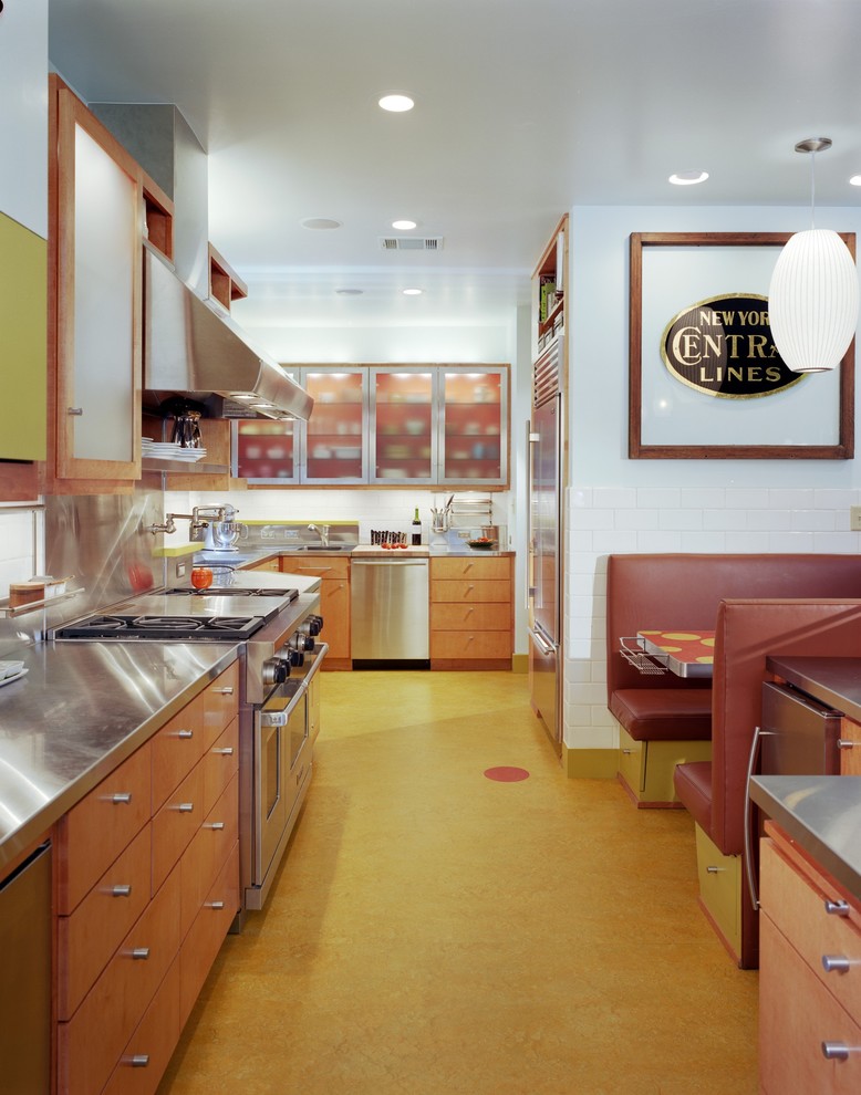 Foto på ett eklektiskt kök, med rostfria vitvaror, bänkskiva i rostfritt stål, släta luckor, skåp i mellenmörkt trä, stänkskydd med metallisk yta, stänkskydd i metallkakel och gult golv