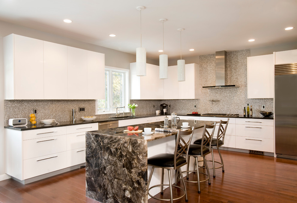 Inredning av ett modernt stort u-kök, med stänkskydd i mosaik, rostfria vitvaror, släta luckor, vita skåp, mellanmörkt trägolv, en köksö, en undermonterad diskho, bänkskiva i kvarts och grått stänkskydd