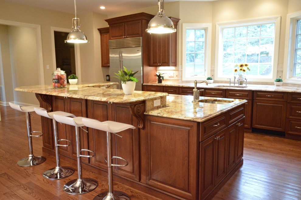 Inspiration for a large transitional medium tone wood floor kitchen remodel in New York with an undermount sink, raised-panel cabinets, dark wood cabinets, granite countertops, beige backsplash, ceramic backsplash and stainless steel appliances