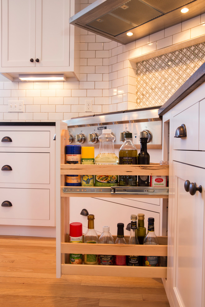 Inspiration for a large cottage l-shaped light wood floor eat-in kitchen remodel in Boston with a farmhouse sink, flat-panel cabinets, white cabinets, granite countertops, white backsplash, subway tile backsplash, stainless steel appliances and an island