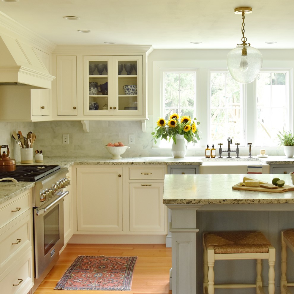 Foto på ett kök, med en rustik diskho, luckor med profilerade fronter, granitbänkskiva, stänkskydd i marmor, integrerade vitvaror, ljust trägolv och en köksö