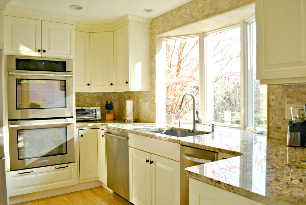 Mid-sized elegant l-shaped light wood floor eat-in kitchen photo in Boston with an undermount sink, raised-panel cabinets, white cabinets, granite countertops, beige backsplash, stone tile backsplash, stainless steel appliances and an island