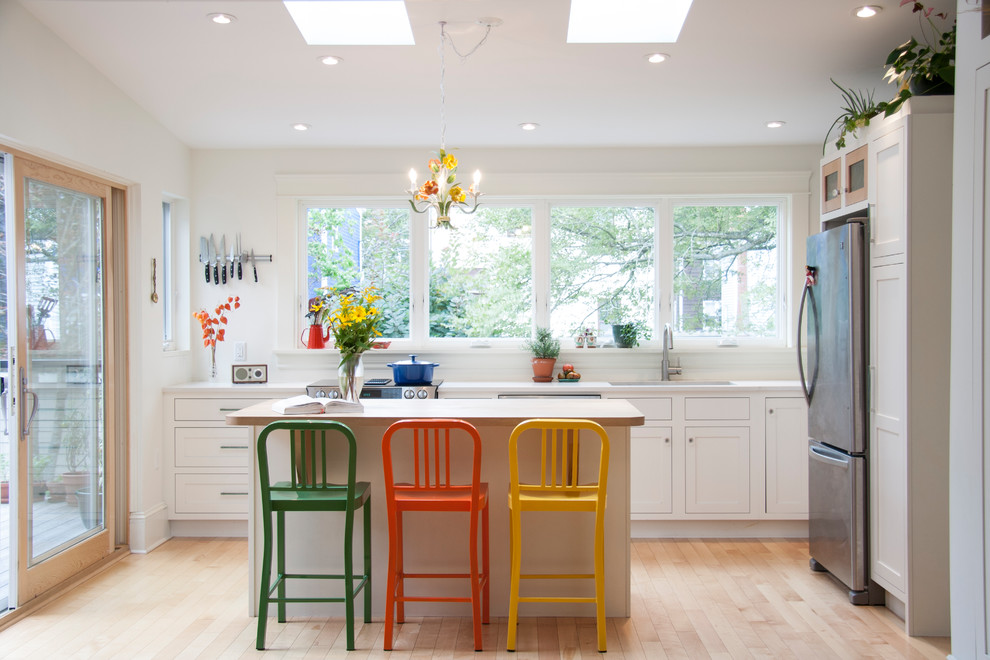Klassisk inredning av ett avskilt, mellanstort l-kök, med en undermonterad diskho, skåp i shakerstil, vita skåp, rostfria vitvaror, ljust trägolv, en köksö, marmorbänkskiva och brunt golv