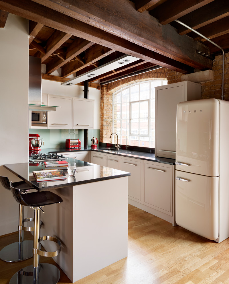 Example of a small eclectic u-shaped light wood floor kitchen design in London with an undermount sink, flat-panel cabinets, beige cabinets, glass sheet backsplash, white appliances and a peninsula