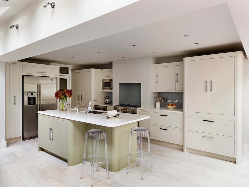 This is an example of a medium sized contemporary l-shaped kitchen in London with a submerged sink, flat-panel cabinets, beige cabinets, grey splashback, glass sheet splashback, stainless steel appliances and an island.