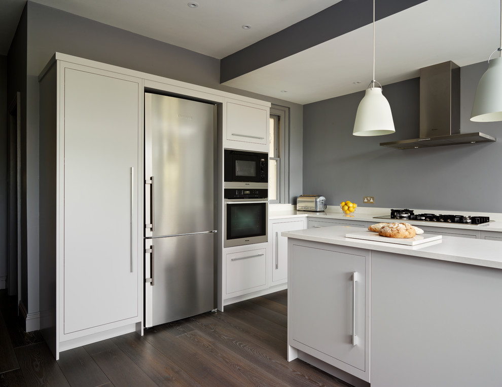Moderne Küche in grau-weiß in L-Form mit flächenbündigen Schrankfronten, weißen Schränken, Küchengeräten aus Edelstahl, dunklem Holzboden und Kücheninsel in London