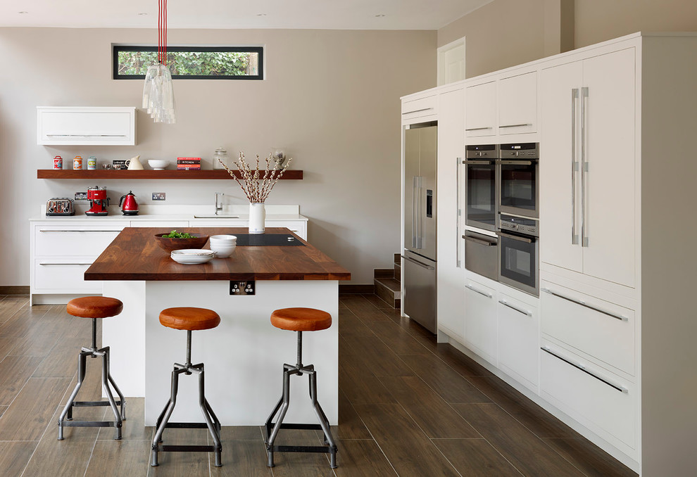 Scandi kitchen in London with a submerged sink, flat-panel cabinets, white cabinets, wood worktops, stainless steel appliances, dark hardwood flooring and an island.