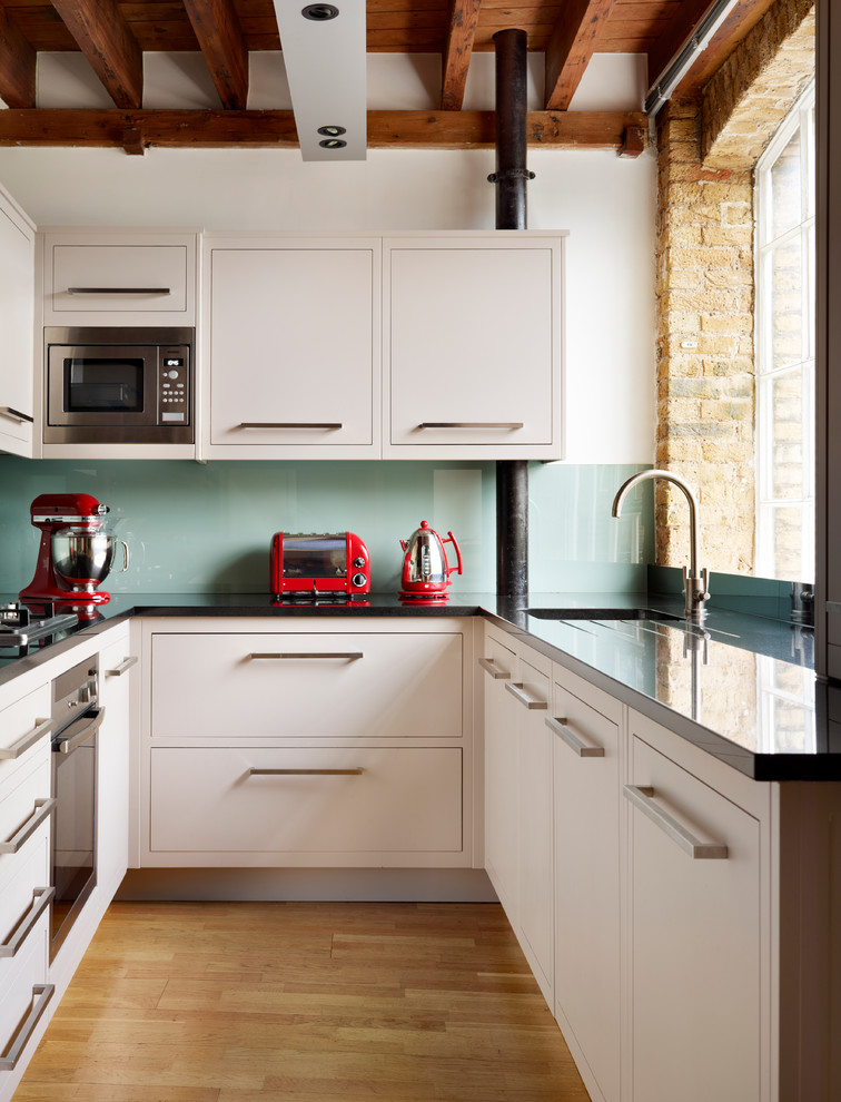 ロンドンにある小さなコンテンポラリースタイルのおしゃれなコの字型キッチン (フラットパネル扉のキャビネット、白いキャビネット、緑のキッチンパネル、ガラス板のキッチンパネル、シルバーの調理設備、淡色無垢フローリング、アイランドなし) の写真