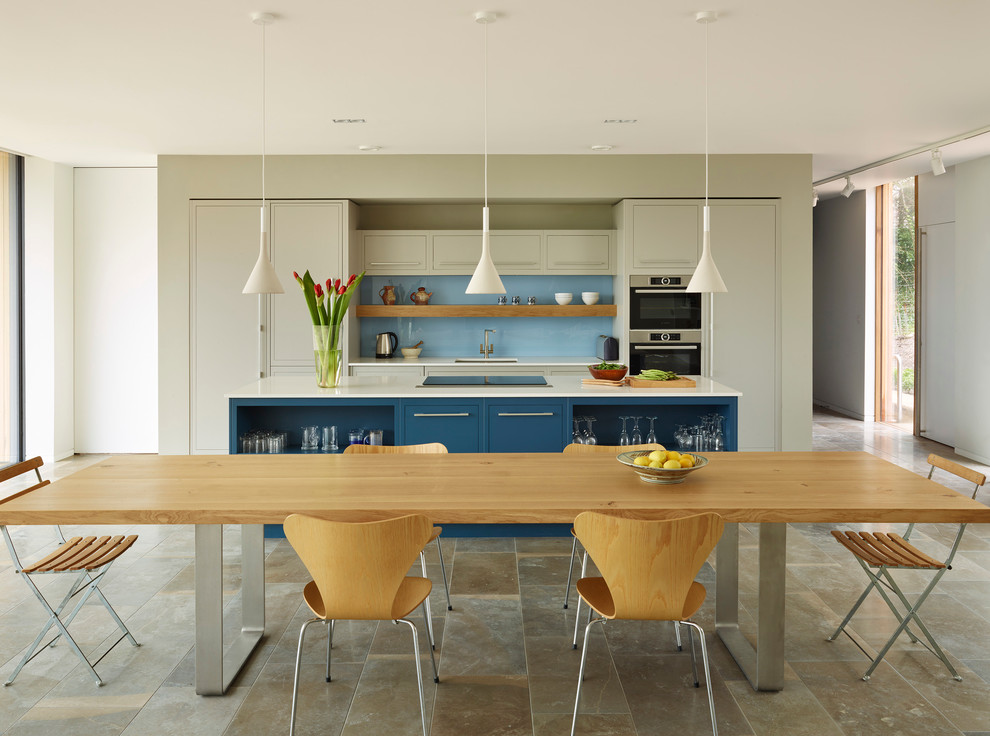 Cette image montre une cuisine américaine design avec un évier encastré, un placard à porte plane, une crédence bleue, une crédence en feuille de verre, un électroménager en acier inoxydable et îlot.