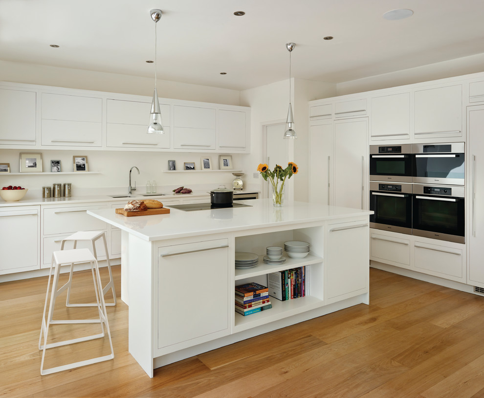 Large danish l-shaped medium tone wood floor kitchen photo in London with an undermount sink, flat-panel cabinets, white cabinets, white backsplash, paneled appliances and an island