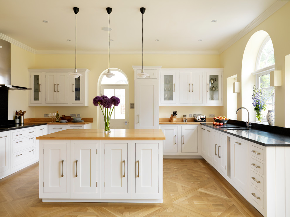 This is an example of a large classic u-shaped kitchen in London with a submerged sink, shaker cabinets, white cabinets, concrete worktops, light hardwood flooring and an island.