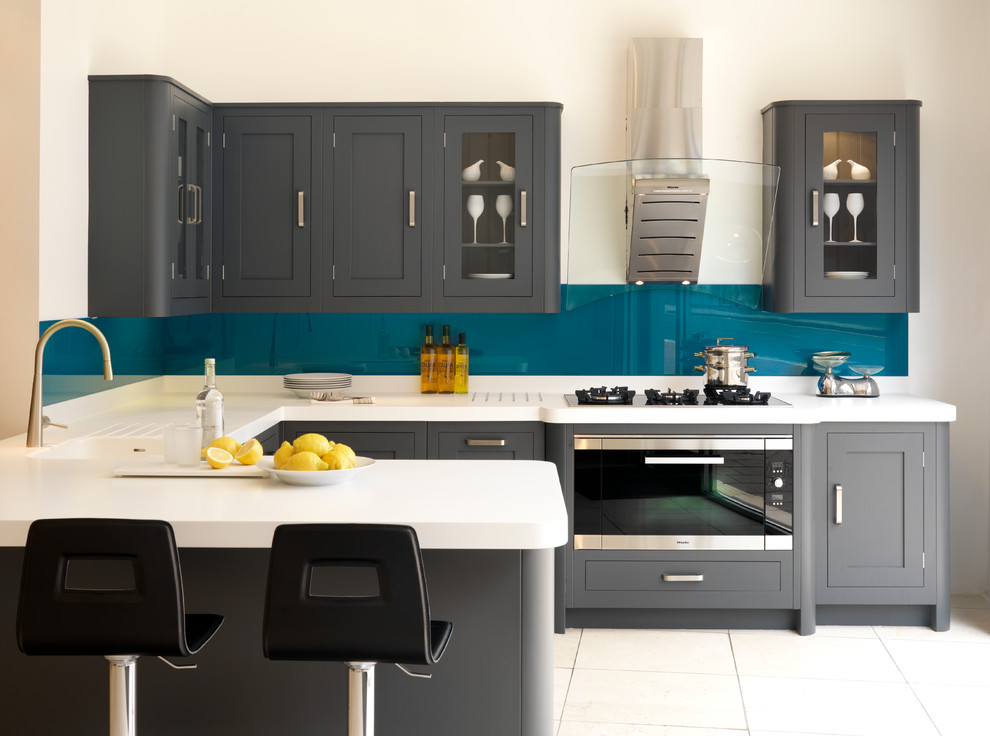 Modelo de cocinas en U gris y blanco clásico renovado con fregadero integrado, armarios estilo shaker, puertas de armario grises, salpicadero azul, salpicadero de vidrio templado, electrodomésticos de acero inoxidable, península y barras de cocina
