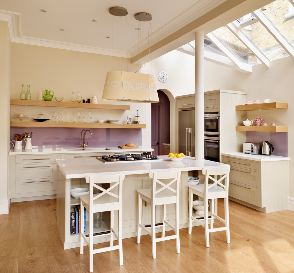 Bild på ett lantligt l-kök, med en undermonterad diskho, öppna hyllor, skåp i ljust trä, glaspanel som stänkskydd, rostfria vitvaror, ljust trägolv och en köksö