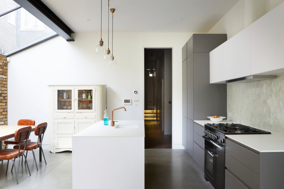 Large contemporary galley kitchen/diner in Other with an integrated sink, flat-panel cabinets, white cabinets, composite countertops, grey splashback, black appliances, concrete flooring, an island, grey floors and white worktops.