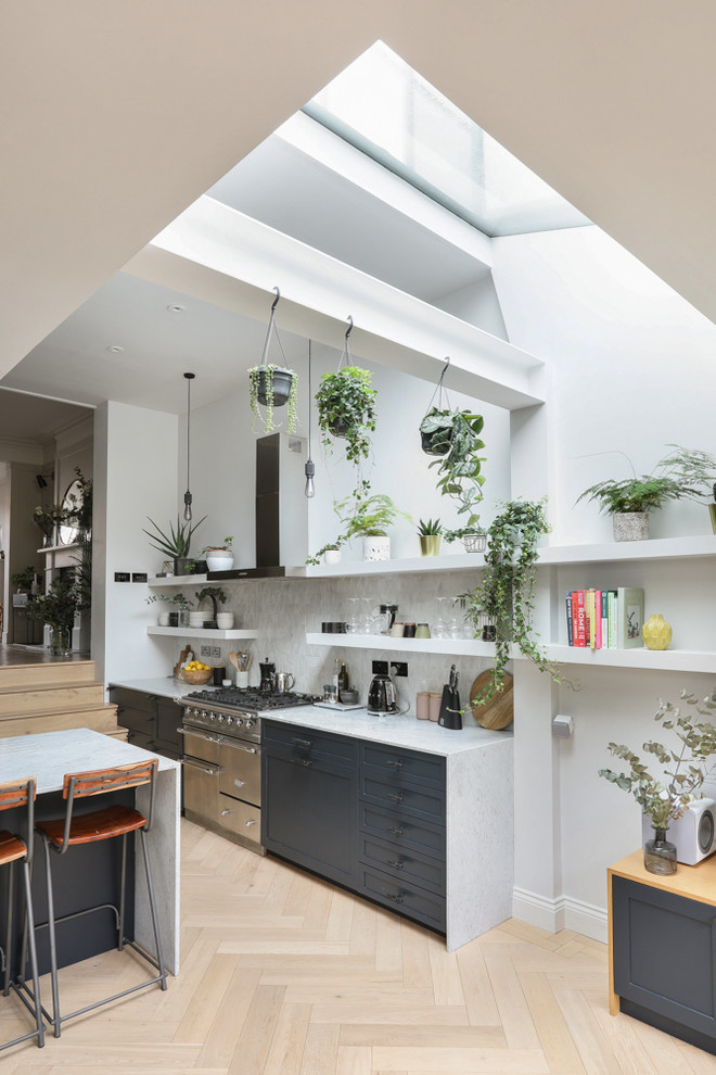 This is an example of a large scandi open plan kitchen in London with an integrated sink, marble worktops, white splashback, ceramic splashback, stainless steel appliances, light hardwood flooring, a breakfast bar, beige floors and white worktops.