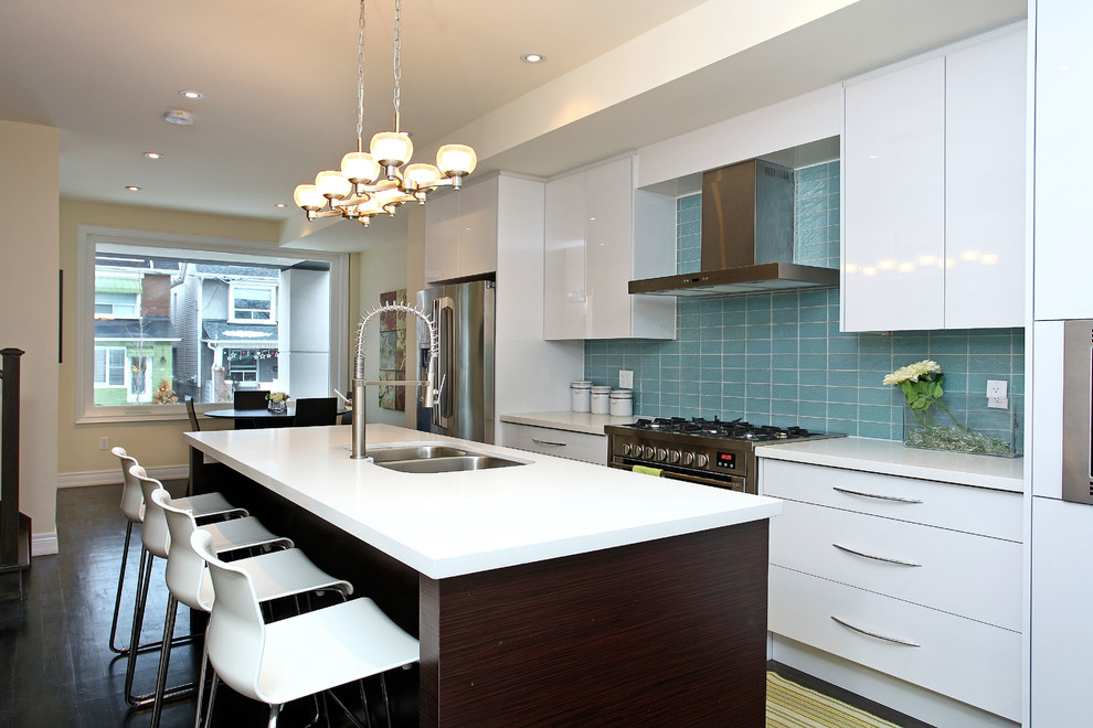 На фото: прямая кухня-гостиная в стиле модернизм с врезной мойкой, плоскими фасадами, белыми фасадами, столешницей из кварцита, синим фартуком, фартуком из стеклянной плитки и техникой из нержавеющей стали