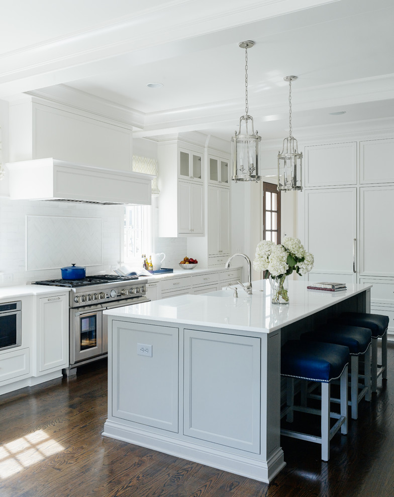 Exempel på ett klassiskt kök, med luckor med infälld panel, vita skåp, vitt stänkskydd, rostfria vitvaror, mörkt trägolv och en köksö