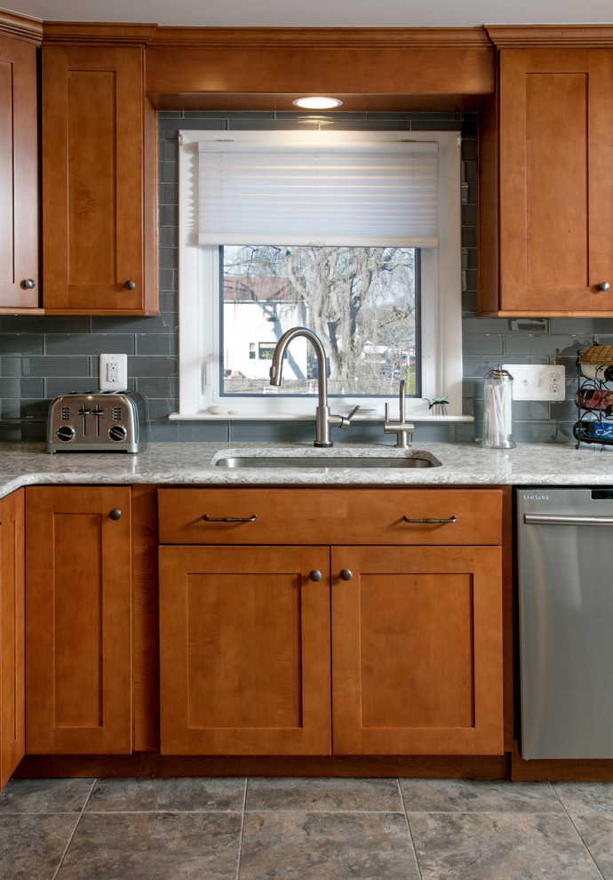 Klassisk inredning av ett avskilt, mellanstort l-kök, med en undermonterad diskho, skåp i shakerstil, skåp i mellenmörkt trä, bänkskiva i kvarts, stänkskydd i glaskakel, rostfria vitvaror, vinylgolv, en köksö, grått stänkskydd och grått golv