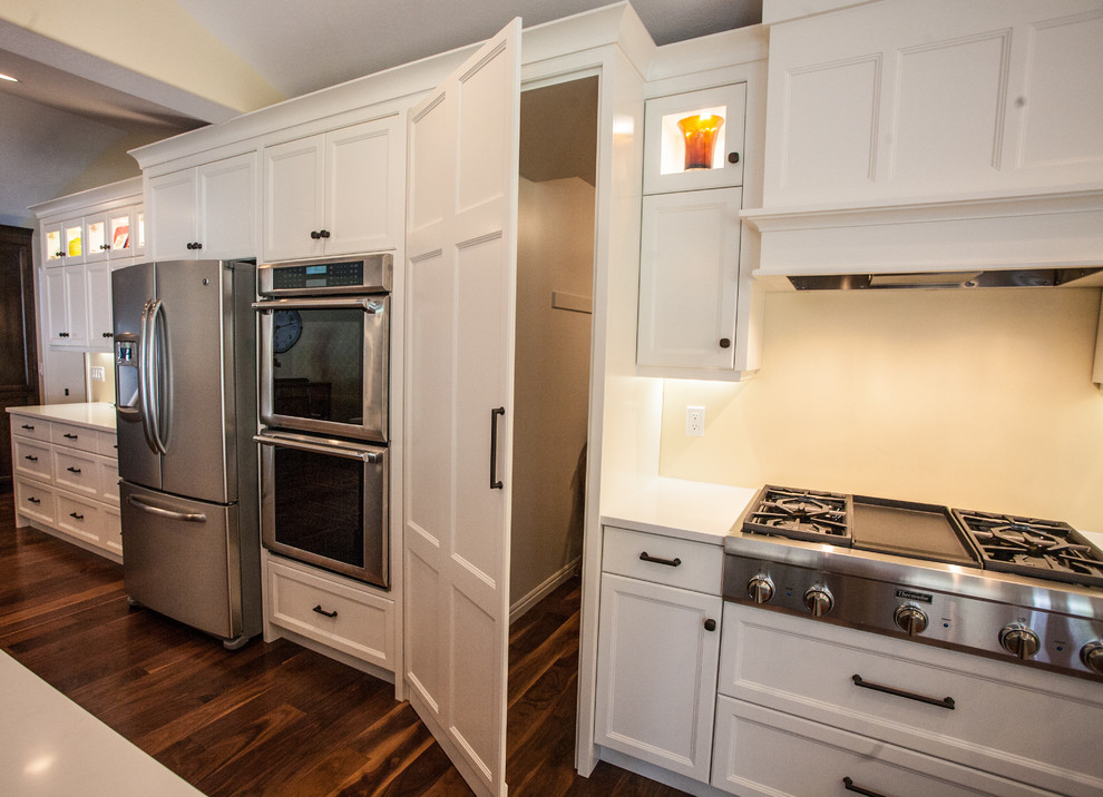 This is an example of a large classic l-shaped kitchen pantry in Salt Lake City with a belfast sink, shaker cabinets, white cabinets, engineered stone countertops, stainless steel appliances, dark hardwood flooring and an island.