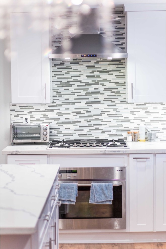 Immagine di una cucina chic di medie dimensioni con lavello a doppia vasca, ante in stile shaker, ante bianche, elettrodomestici in acciaio inossidabile, pavimento in laminato, top in quarzite, paraspruzzi con piastrelle a mosaico e top bianco