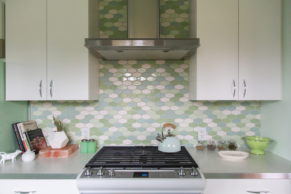 Inredning av ett 60 tals vit vitt kök, med en nedsänkt diskho, släta luckor, vita skåp, laminatbänkskiva, flerfärgad stänkskydd, stänkskydd i keramik, färgglada vitvaror, linoleumgolv och grönt golv