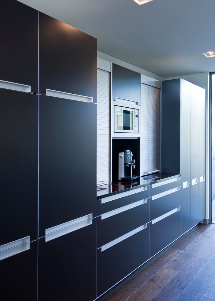 Moderne Wohnküche ohne Insel mit Waschbecken, grauen Schränken, Granit-Arbeitsplatte, Küchenrückwand in Grau, Glasrückwand, bunten Elektrogeräten und dunklem Holzboden in Wellington