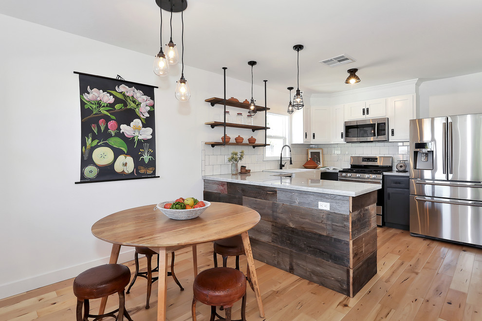 Example of an eclectic u-shaped eat-in kitchen design in Los Angeles with a farmhouse sink, shaker cabinets, white cabinets, white backsplash and stainless steel appliances