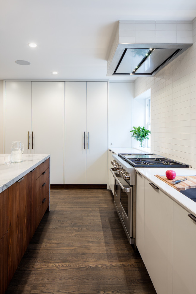 Eat-in kitchen - large modern l-shaped medium tone wood floor and brown floor eat-in kitchen idea in Philadelphia with an undermount sink, flat-panel cabinets, white cabinets, quartzite countertops, white backsplash, ceramic backsplash, paneled appliances, an island and white countertops