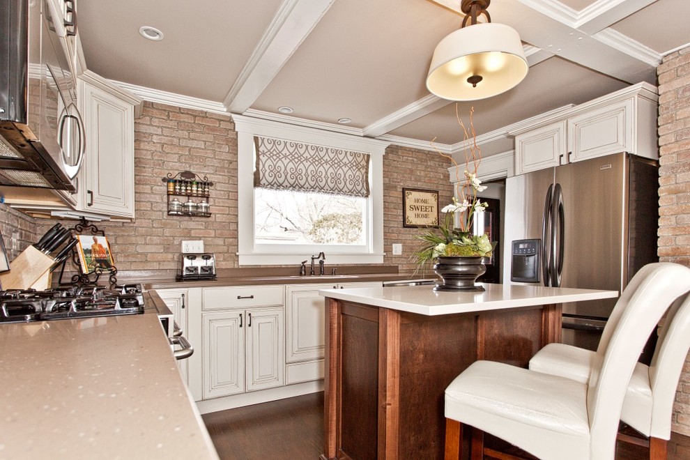 Example of a mid-sized transitional u-shaped brown floor enclosed kitchen design in Boston with an undermount sink, raised-panel cabinets, white cabinets, solid surface countertops, brown backsplash, brick backsplash, stainless steel appliances and an island
