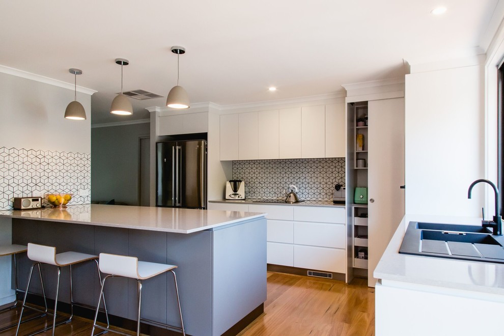 Inspiration for a contemporary galley kitchen in Canberra - Queanbeyan with a built-in sink, white cabinets, engineered stone countertops, multi-coloured splashback, ceramic splashback, black appliances, light hardwood flooring, an island and brown floors.
