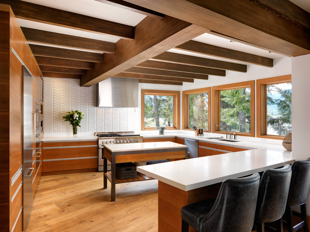 Mountain style u-shaped medium tone wood floor kitchen photo in Vancouver with a double-bowl sink, flat-panel cabinets, medium tone wood cabinets, white backsplash, stainless steel appliances, an island and white countertops