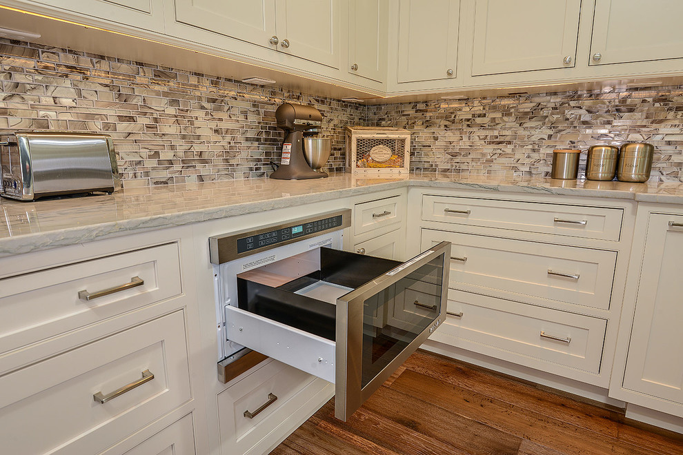 Bild på ett stort vintage kök, med en rustik diskho, luckor med profilerade fronter, vita skåp, bänkskiva i kvartsit, stänkskydd med metallisk yta, stänkskydd i glaskakel, rostfria vitvaror, ljust trägolv och en köksö