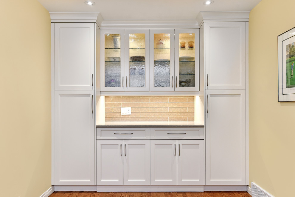 This is an example of a medium sized traditional l-shaped kitchen/diner in Calgary with a submerged sink, recessed-panel cabinets, white cabinets, engineered stone countertops, grey splashback, glass tiled splashback, stainless steel appliances, medium hardwood flooring, an island and beige floors.