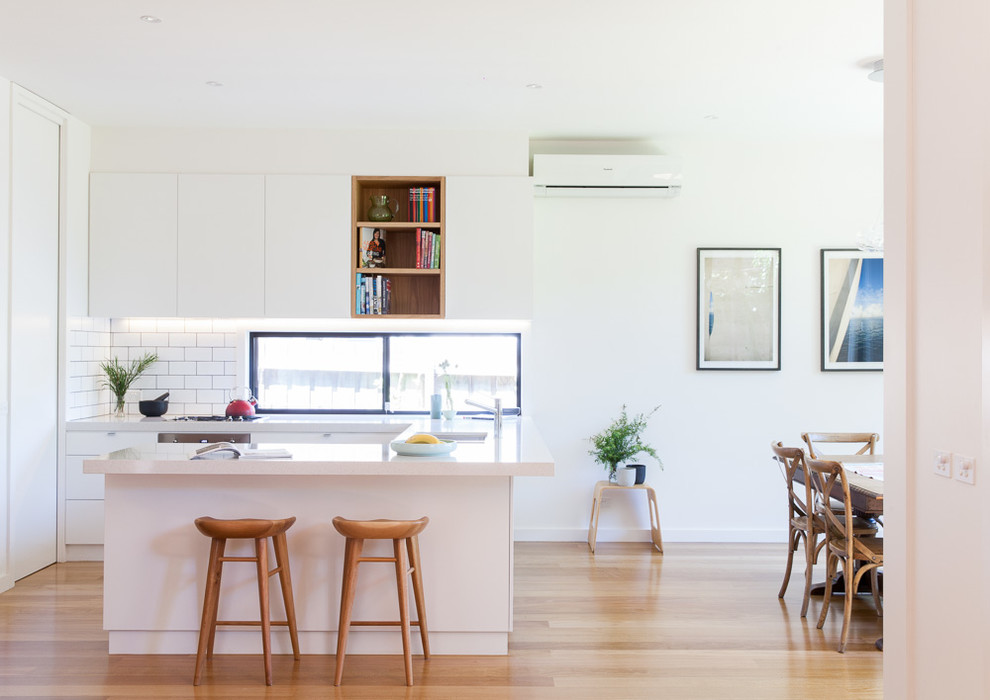 Inspiration for a small contemporary u-shaped kitchen/diner in Melbourne with medium hardwood flooring, a submerged sink, flat-panel cabinets, white cabinets, white splashback, metro tiled splashback and a breakfast bar.