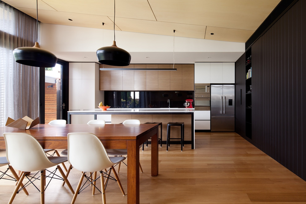 Moderne Wohnküche mit flächenbündigen Schrankfronten, Küchenrückwand in Schwarz, Glasrückwand, Küchengeräten aus Edelstahl, braunem Holzboden und Kücheninsel in Melbourne