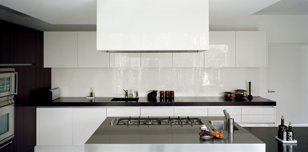 Cette image montre une grande cuisine américaine design avec un plan de travail en surface solide, une crédence blanche, une crédence en feuille de verre, un électroménager en acier inoxydable, sol en béton ciré et îlot.
