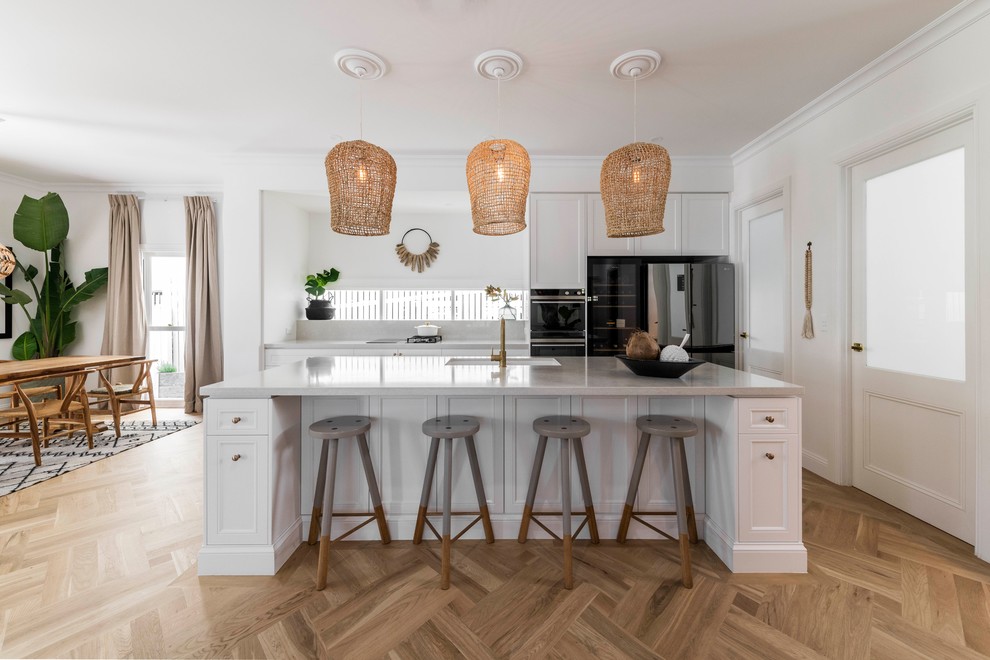 Eat-in kitchen - large coastal galley medium tone wood floor and beige floor eat-in kitchen idea in Brisbane with an undermount sink, marble countertops, white backsplash, marble backsplash, an island, white countertops, recessed-panel cabinets, white cabinets and black appliances