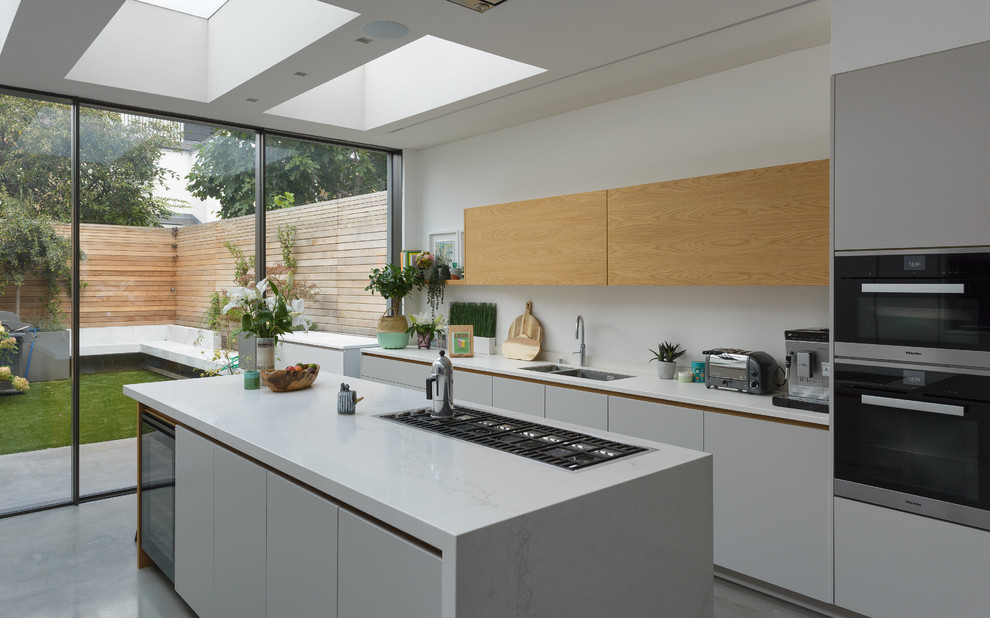 Design ideas for a medium sized contemporary galley open plan kitchen in London with an integrated sink, flat-panel cabinets, grey cabinets, composite countertops, white splashback, integrated appliances, concrete flooring, an island and grey floors.