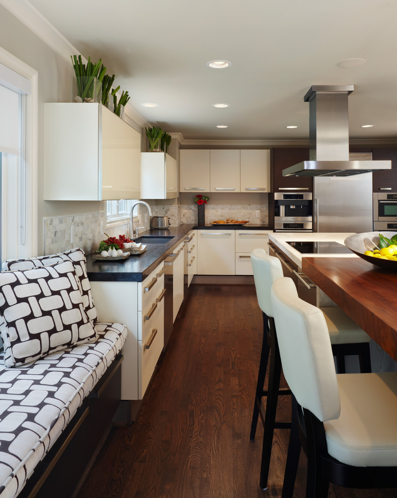 Inspiration for a mid-sized transitional u-shaped dark wood floor eat-in kitchen remodel in Detroit with an undermount sink, flat-panel cabinets, white cabinets, white backsplash, stainless steel appliances, solid surface countertops, stone tile backsplash and an island