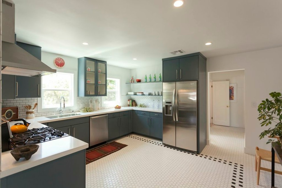 Modelo de cocinas en U bohemio cerrado con puertas de armario azules, salpicadero blanco, salpicadero de azulejos tipo metro y electrodomésticos de acero inoxidable