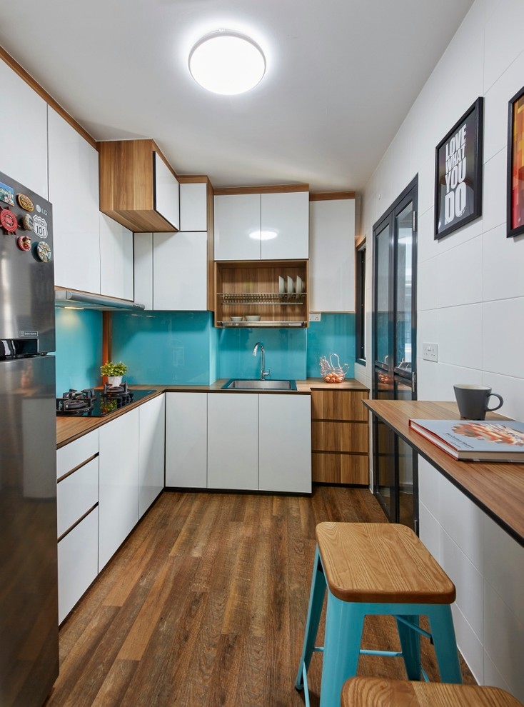 Small contemporary l-shaped kitchen in Singapore with a single-bowl sink, flat-panel cabinets, white cabinets, wood worktops, blue splashback, glass sheet splashback, medium hardwood flooring and no island.