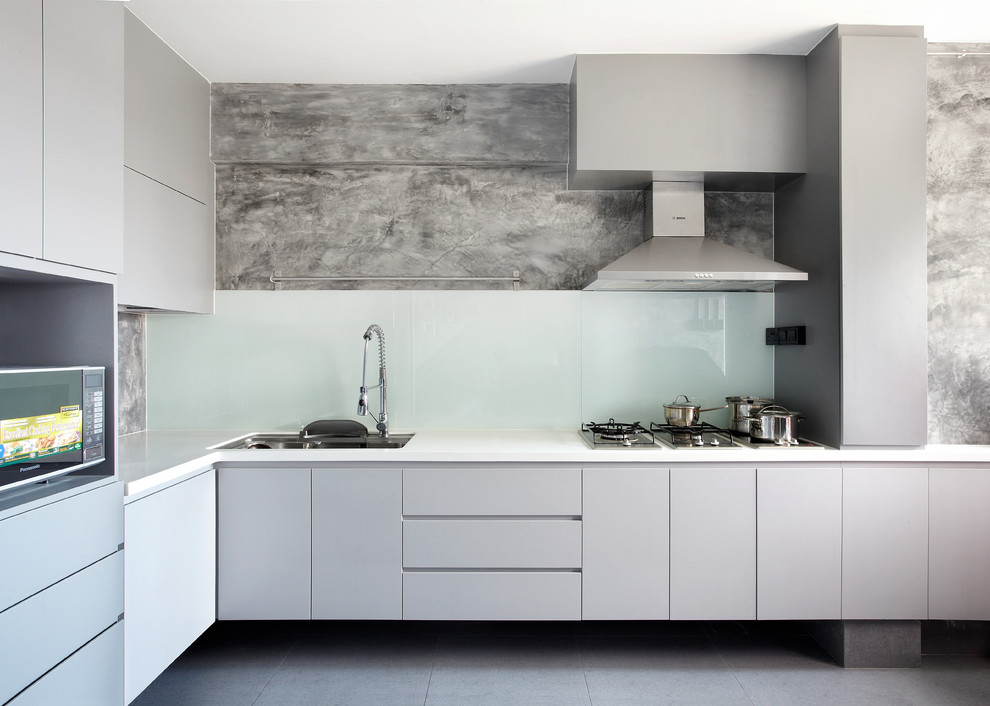 Идея дизайна: угловая кухня в современном стиле с врезной мойкой, плоскими фасадами, серыми фасадами, белым фартуком, фартуком из стекла, техникой из нержавеющей стали, серым полом и белой столешницей