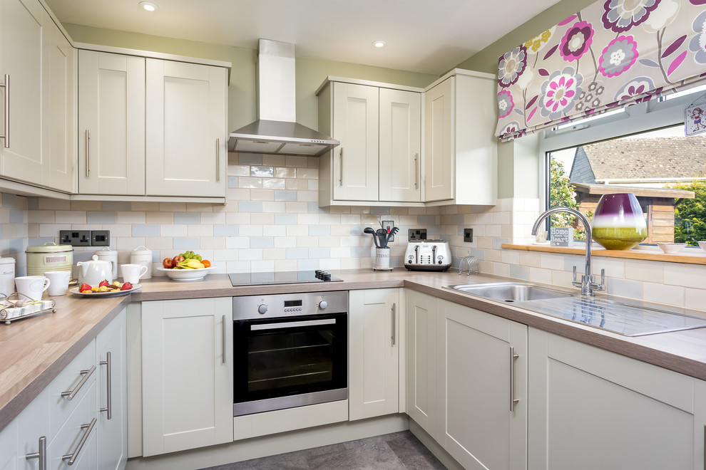 This is an example of a small classic u-shaped enclosed kitchen in Gloucestershire with a built-in sink, shaker cabinets, green cabinets, wood worktops, beige splashback, mosaic tiled splashback, stainless steel appliances, ceramic flooring and no island.