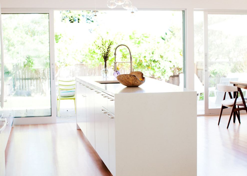 Example of a small minimalist galley light wood floor eat-in kitchen design in San Francisco with an undermount sink, flat-panel cabinets, white cabinets, quartz countertops, gray backsplash, porcelain backsplash, white appliances and an island